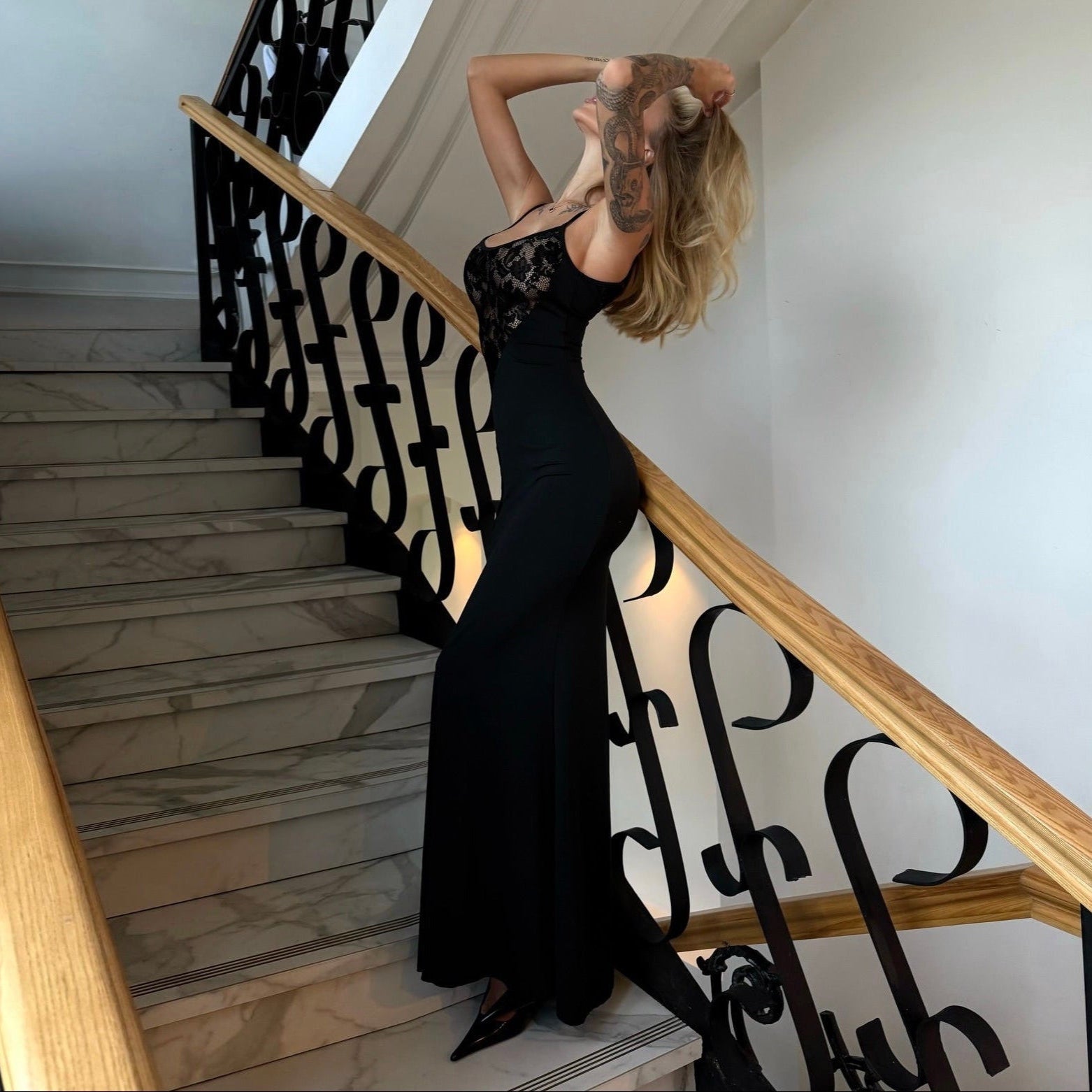 Woman in a black dress standing on a staircase with decorative railings.