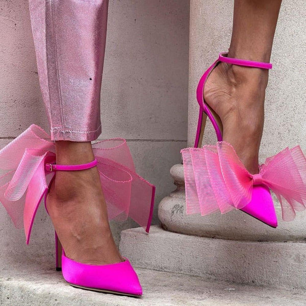 Pink high-heeled shoes with tulle bows worn by a person on a stone step.