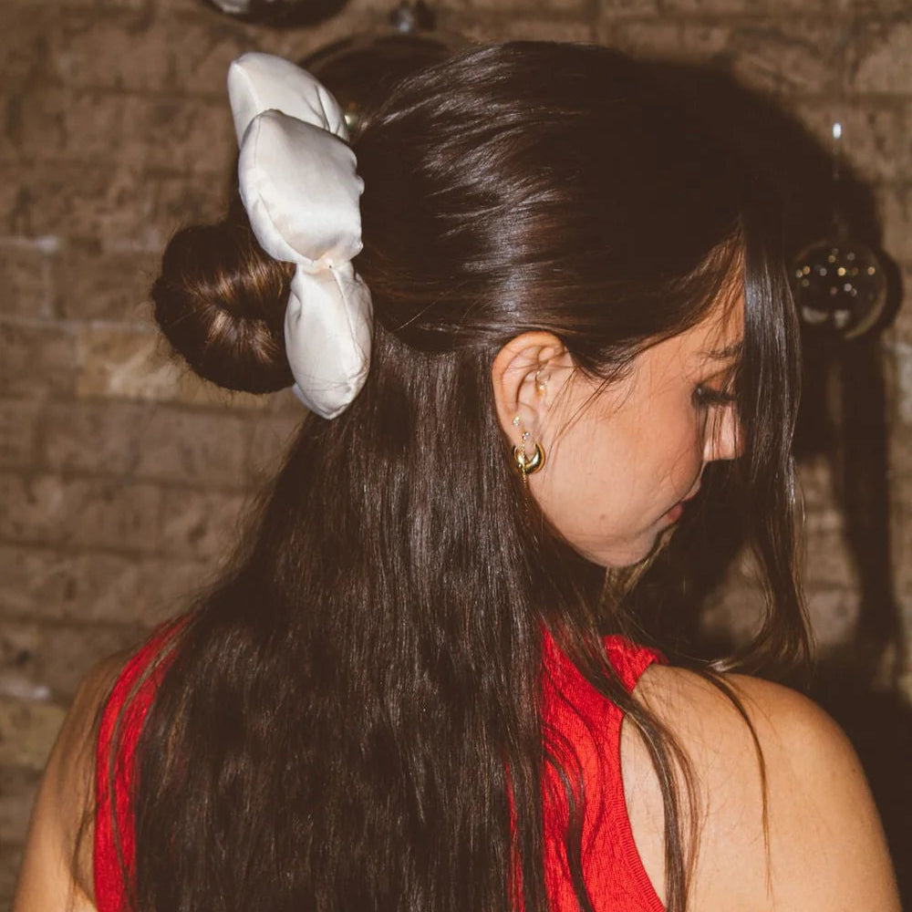 Woman with long dark hair styled in a bun with a white bow, wearing a red top.