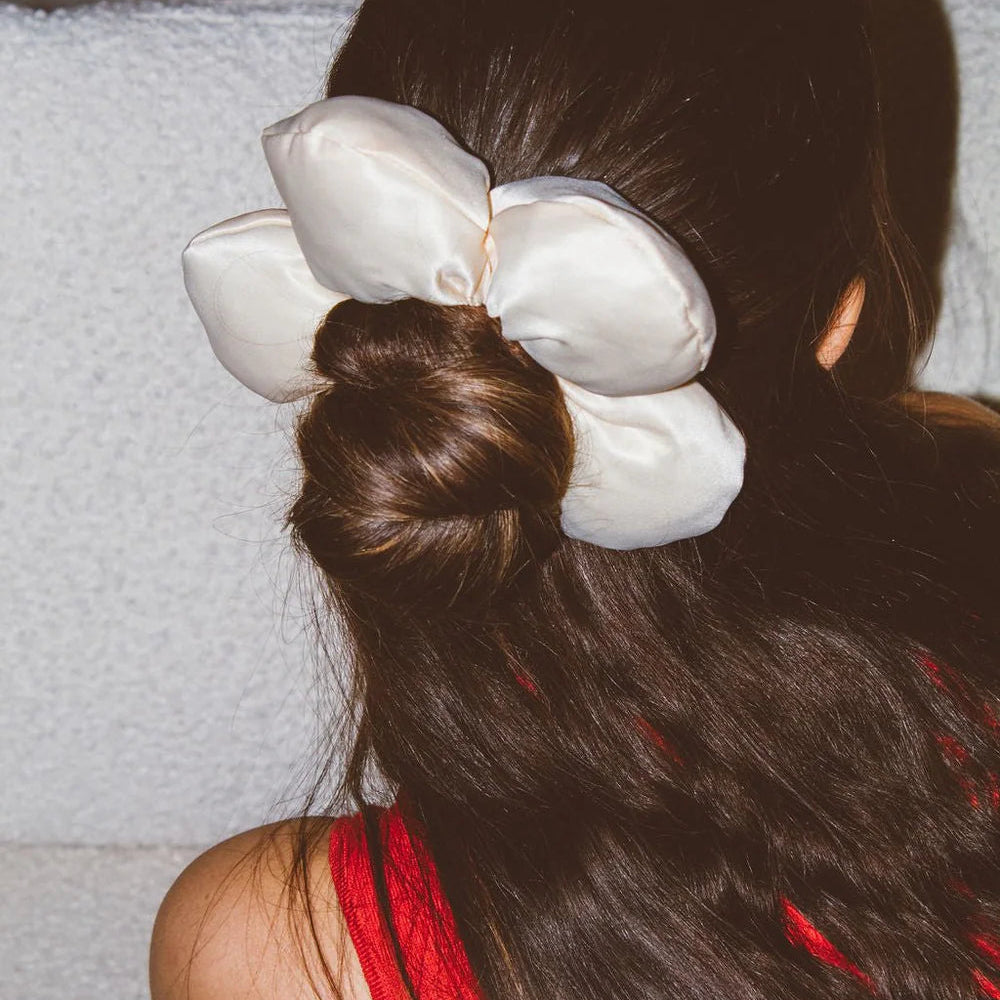 Person with long dark hair styled in a bun with a large white flower accessory, wearing a red top.