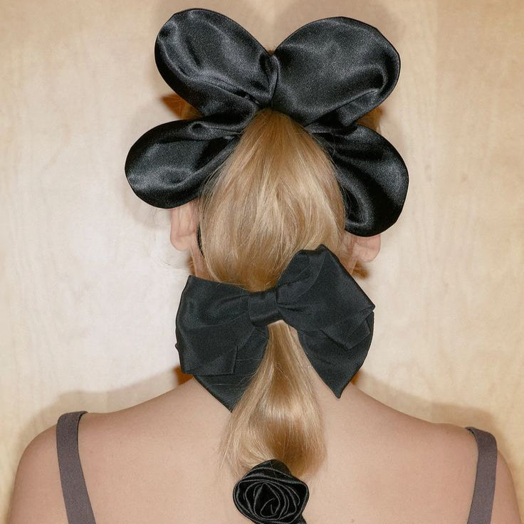 Person with black satin hair bows styled in a ponytail against a beige background