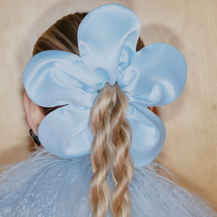 Person with braided hair wearing a large light blue bow against a neutral background