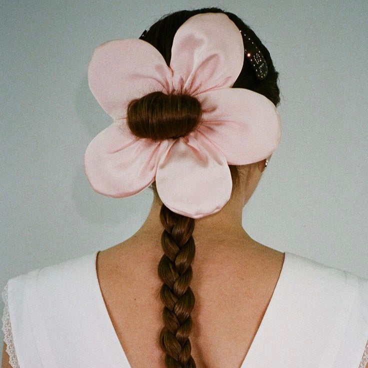 Person with braided hair wearing a large pink flower headpiece against a neutral background