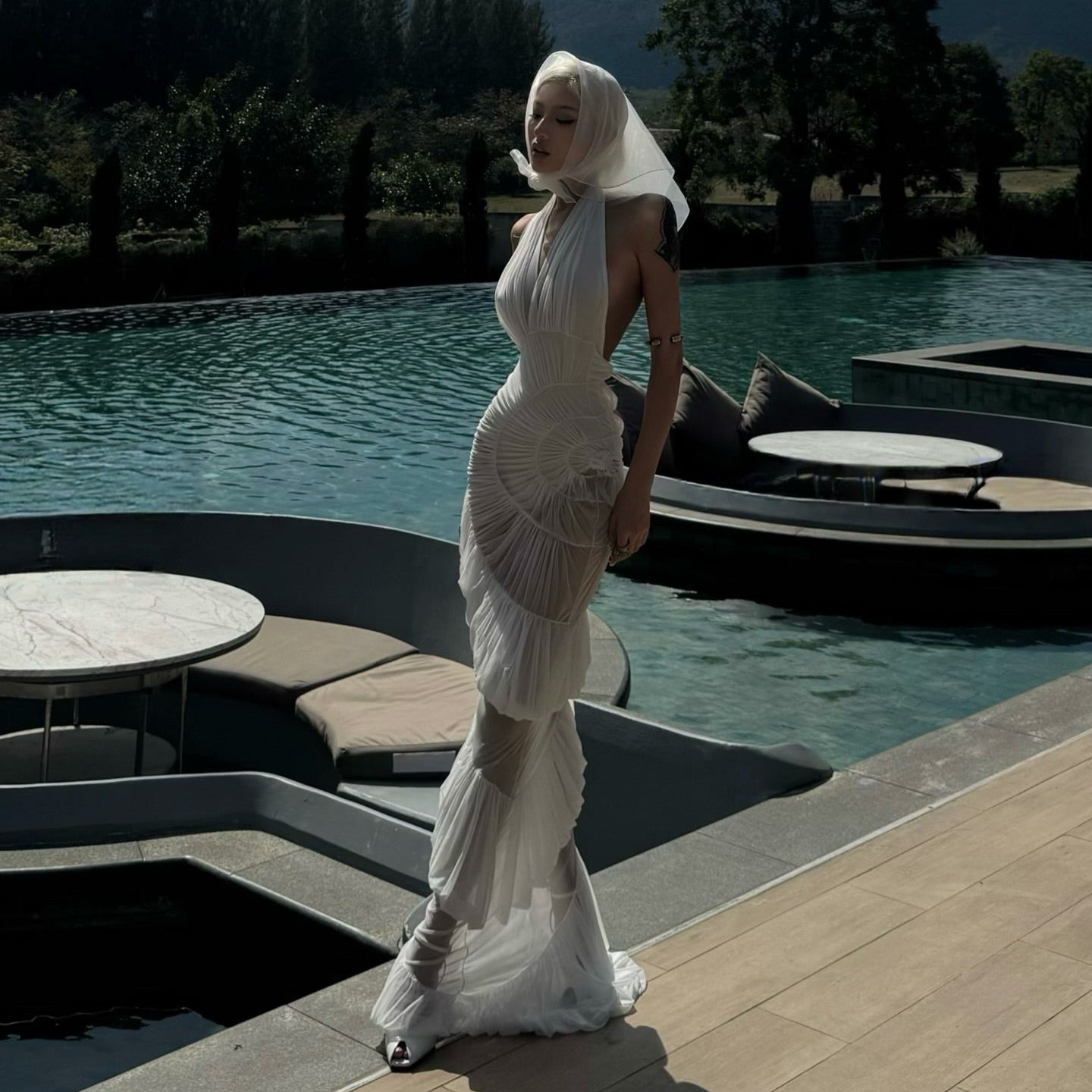 Woman in a white dress standing by a pool with mountains in the background