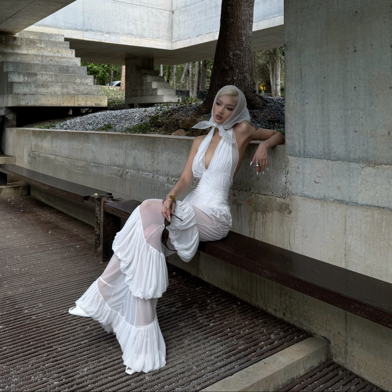 Woman in a white dress sitting on a concrete bench with a modern architectural background
