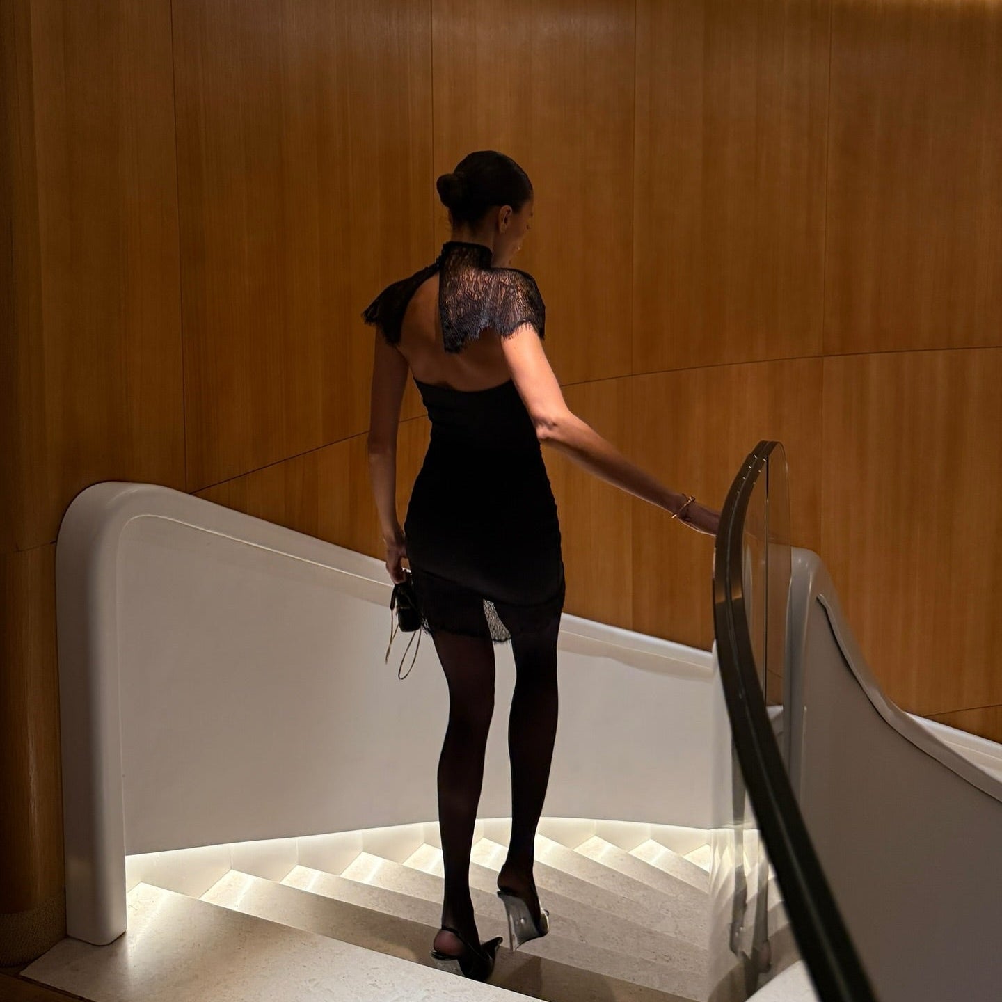 Woman in a black dress standing on a modern staircase with wooden walls.