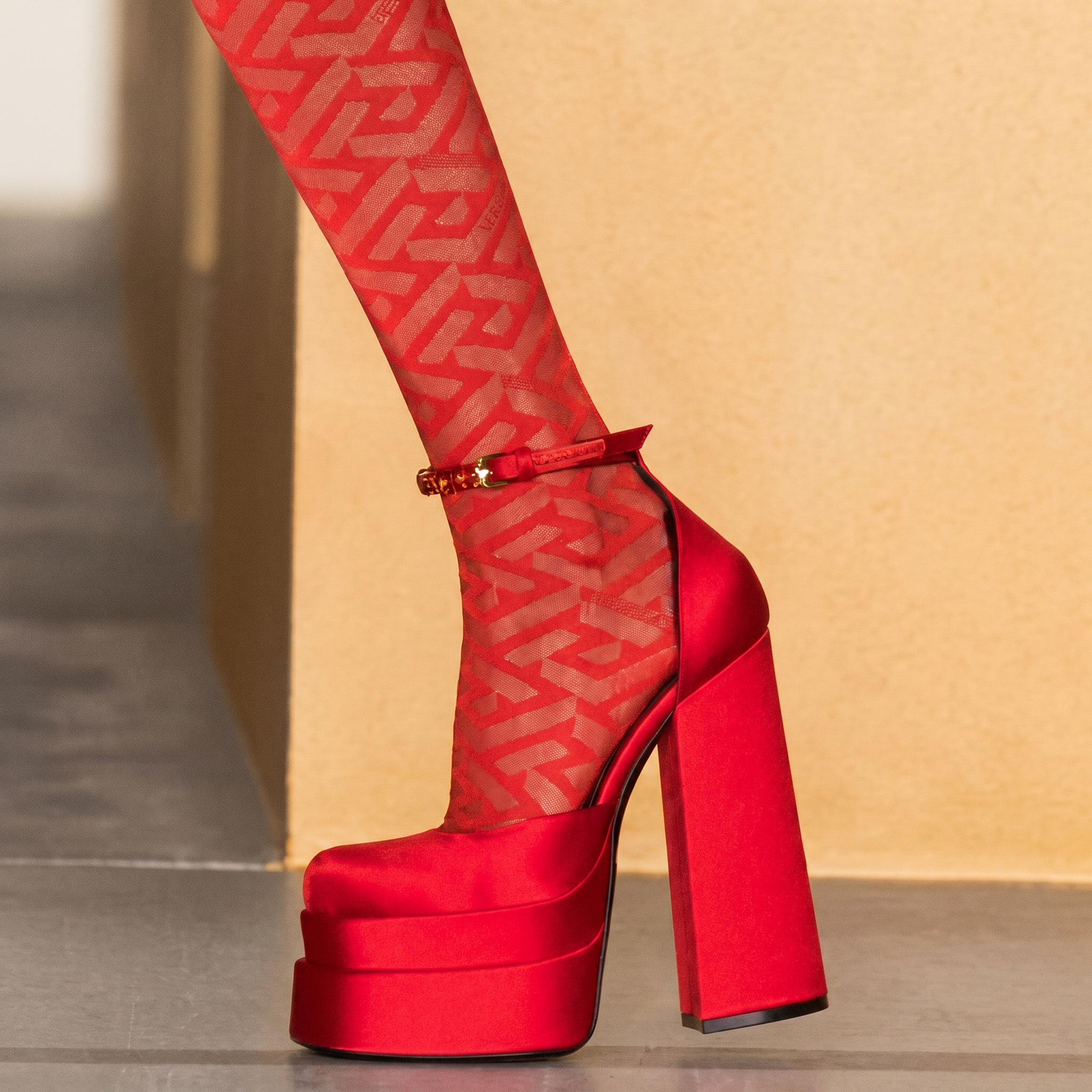 Red platform high heel shoe with matching red patterned tights on a neutral background
