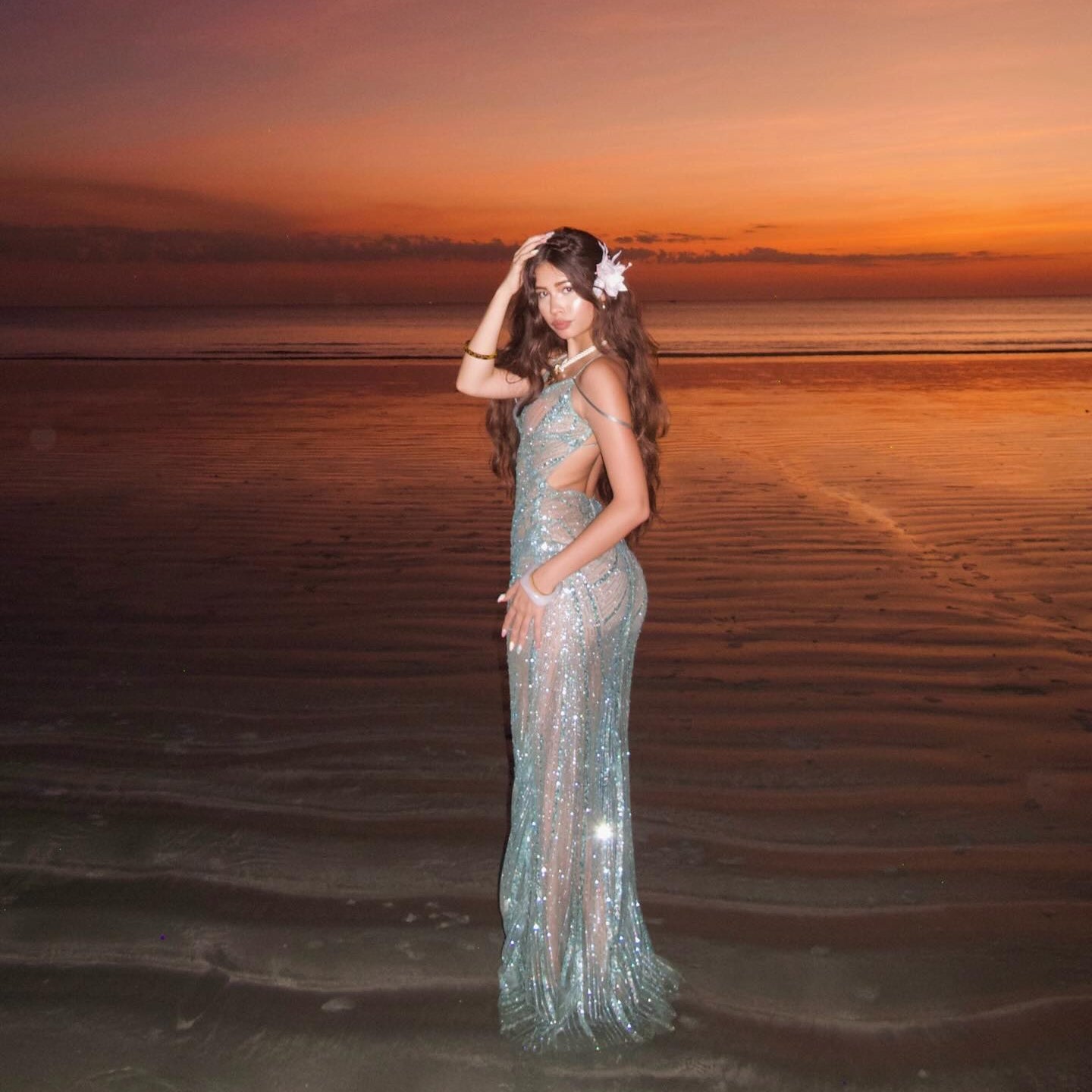 Woman in a sparkly dress standing on a beach at sunset