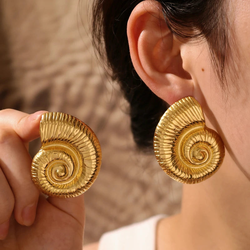 Gold spiral earrings being worn and held up to the ear against a neutral background
