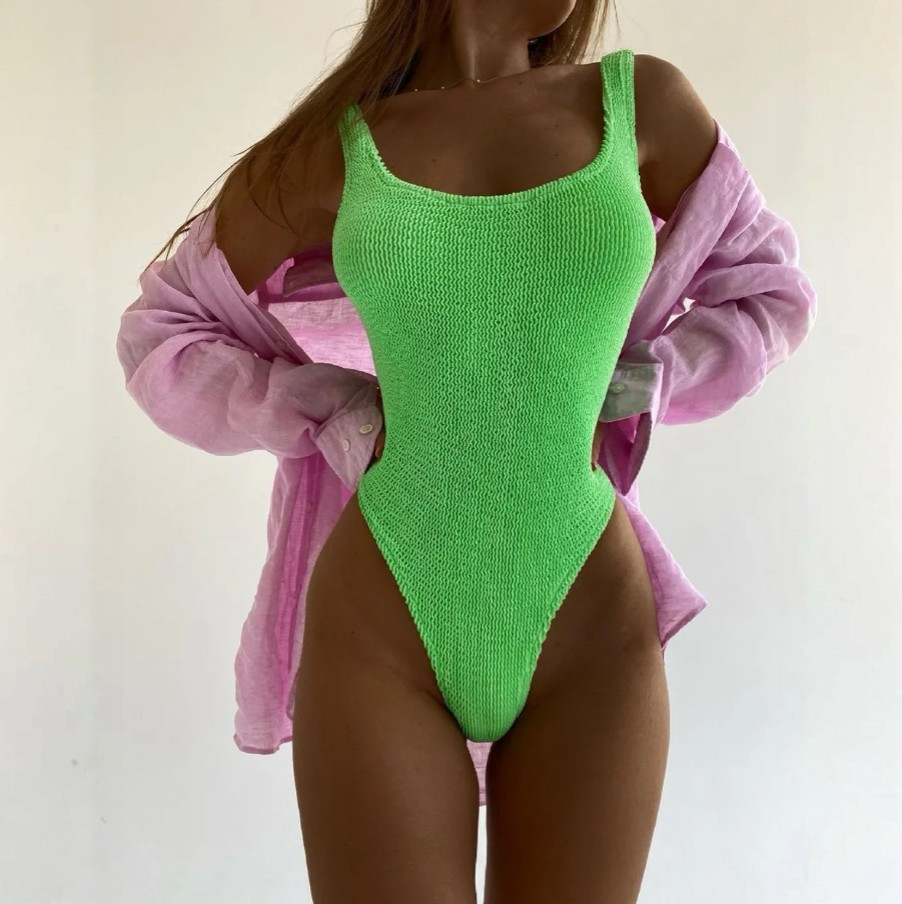 Person wearing a green swimsuit with a pink shirt over the shoulders on a plain background