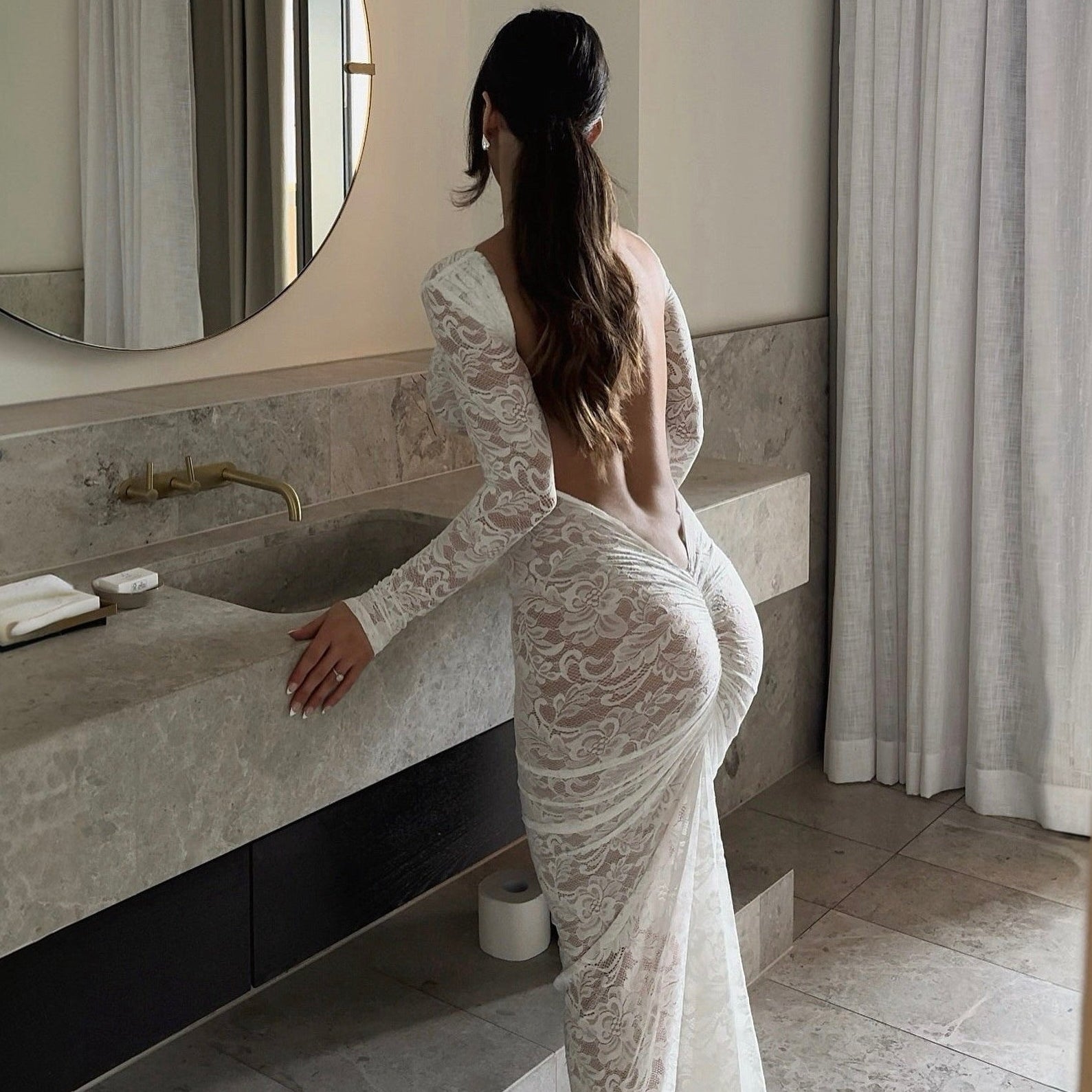 Woman in a white lace dress standing in a bathroom.