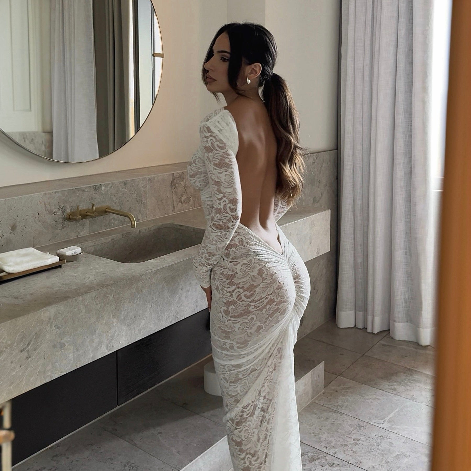 Woman in a white lace dress standing in a bathroom.