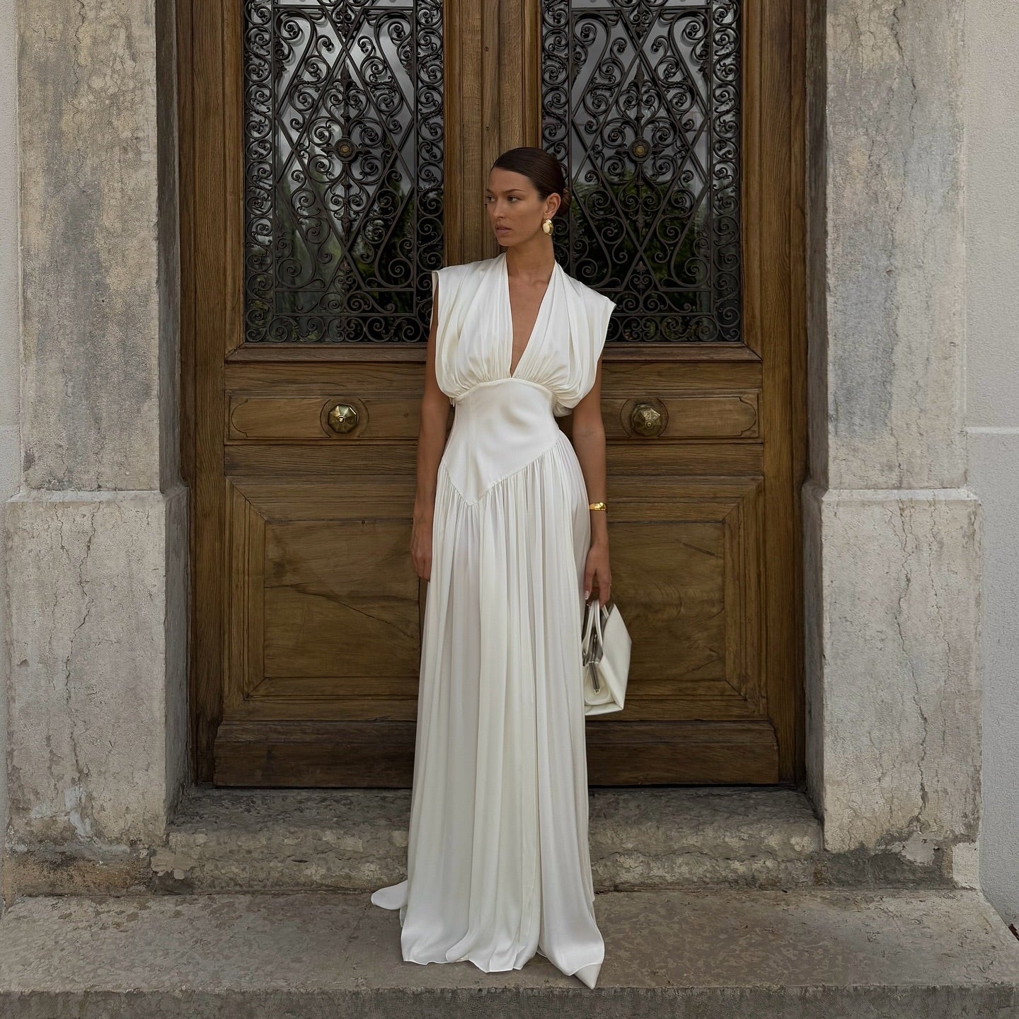 Woman in a white dress standing in front of a wooden door with decorative glass panels.