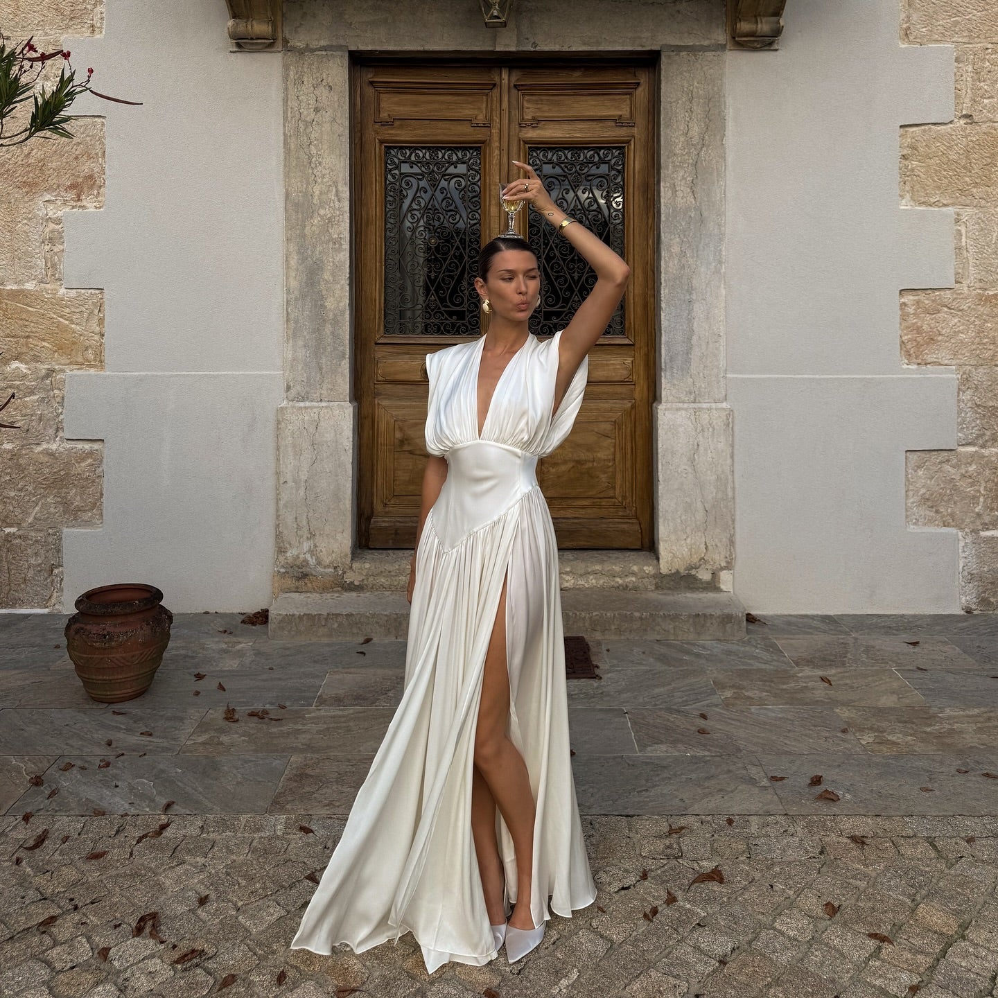 Woman in a white dress standing in front of a stone building with wooden doors.