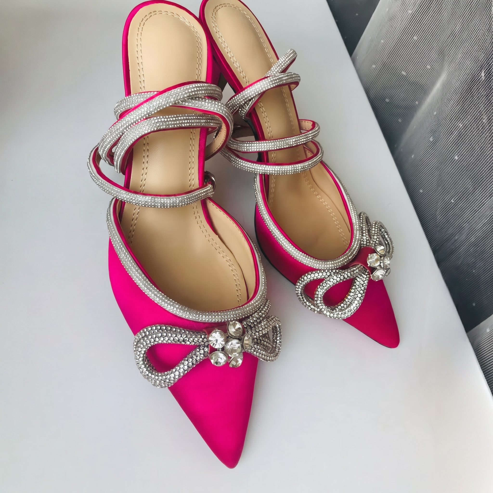 Pink high-heeled shoes with silver embellishments on a white surface.