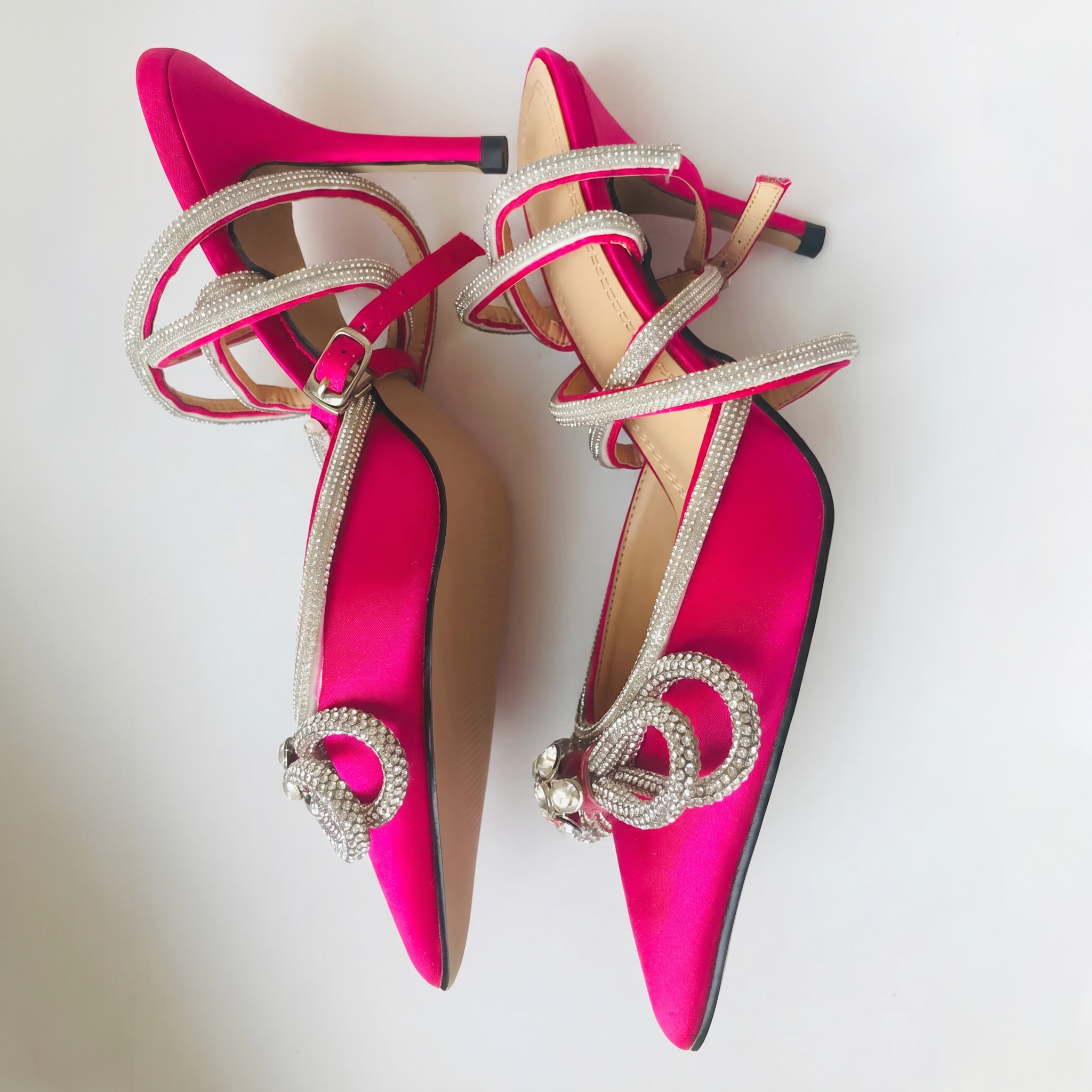 Pair of pink high-heeled shoes with decorative straps on a white background