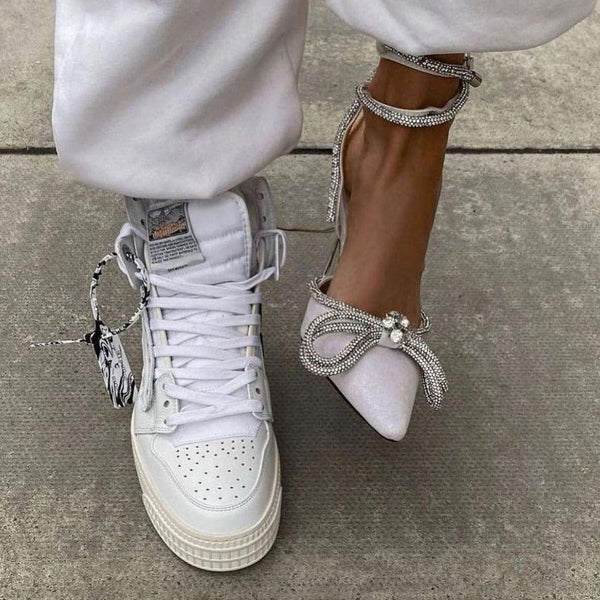 White heels with decorative laces and embellishments on a concrete surface.