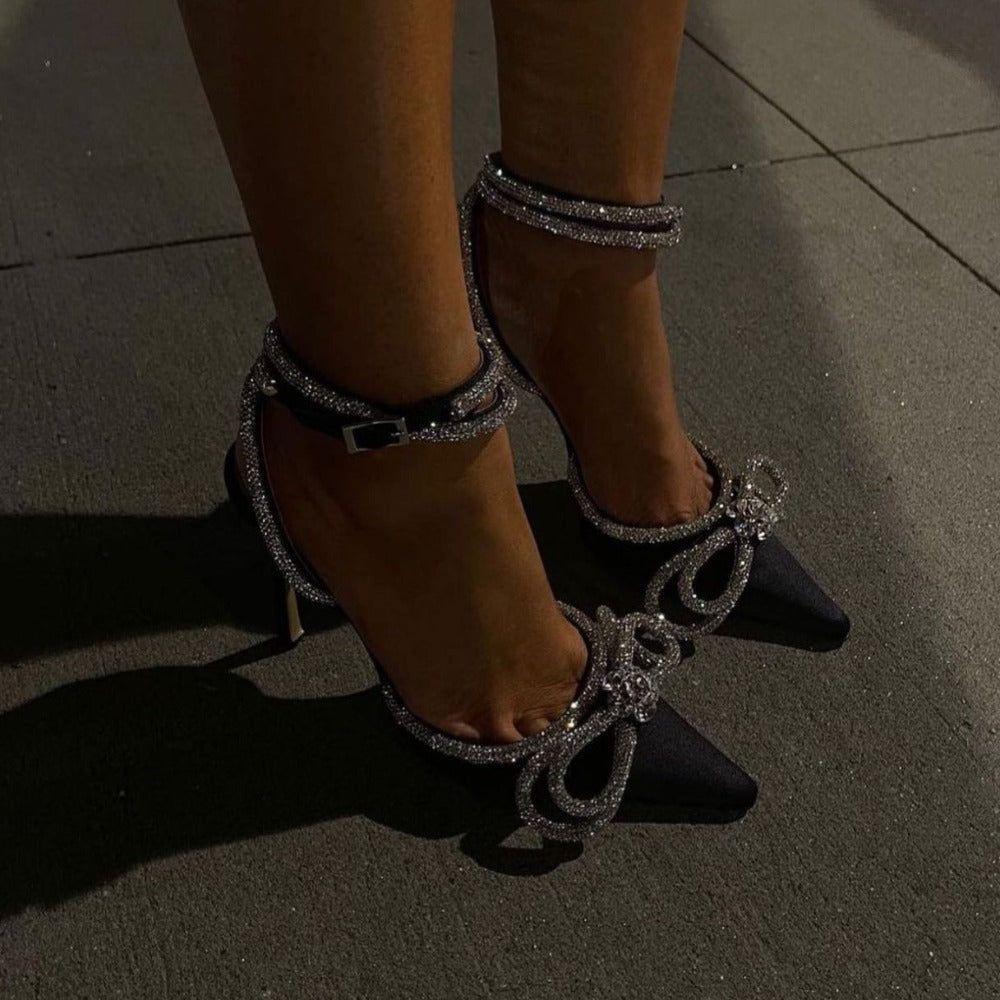 Black high-heeled shoes with silver embellishments on a tiled floor.