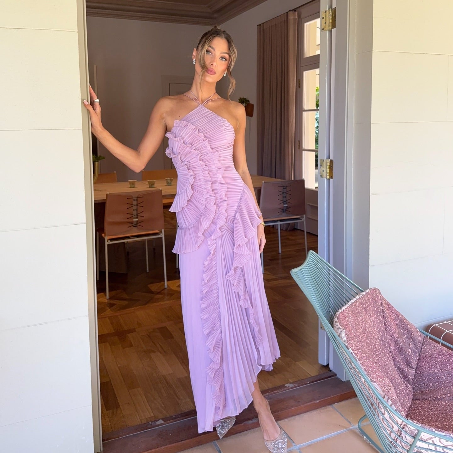 Woman in a pink dress standing in a doorway with a chair and table in the background.