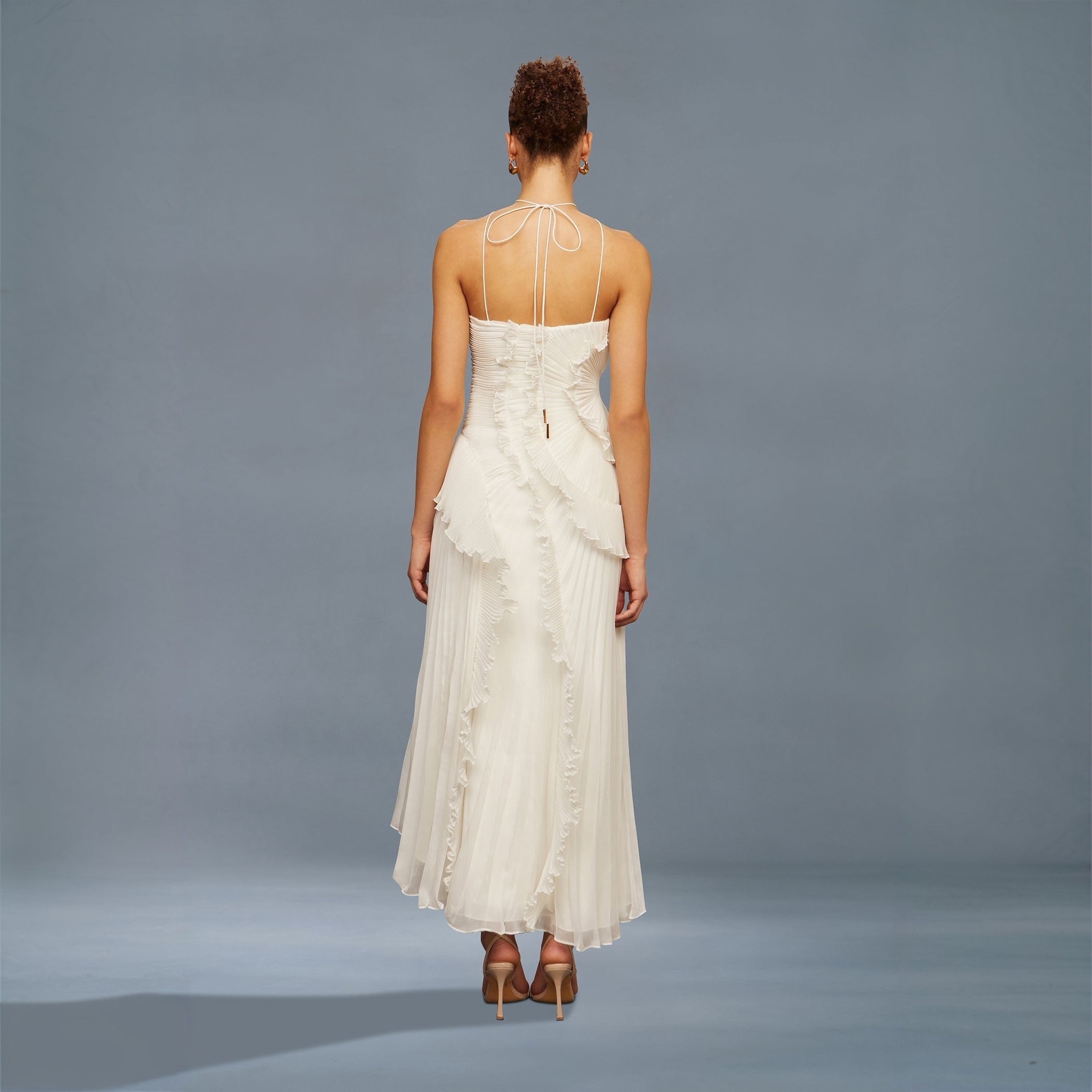 Woman wearing a white dress with thin straps against a gray background