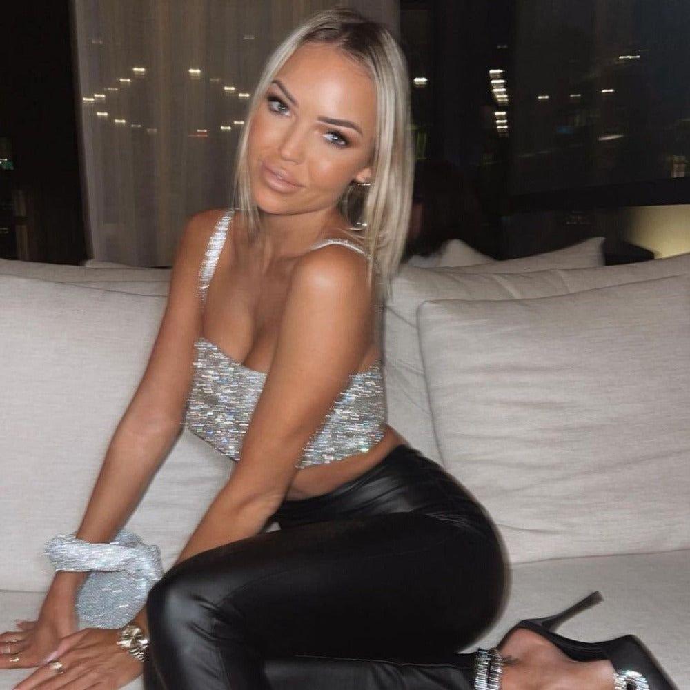 Woman in a silver top and black pants sitting on a couch at night.