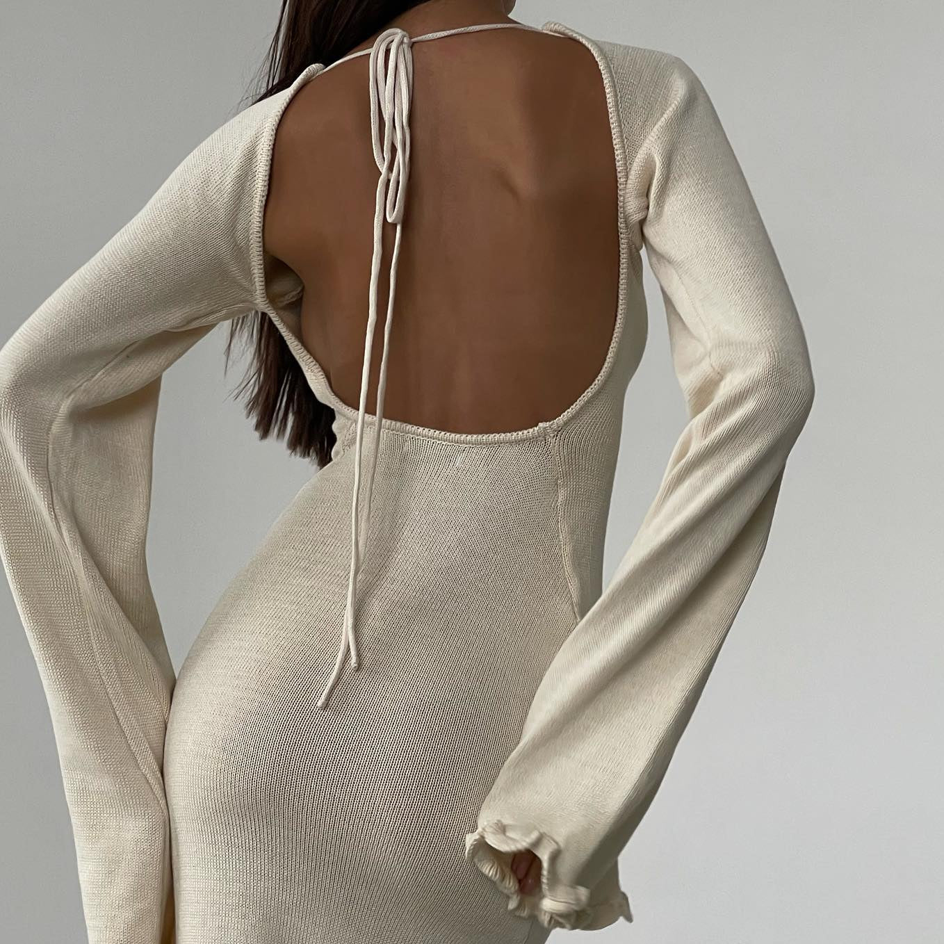 Beige long-sleeve dress with open back on a plain background