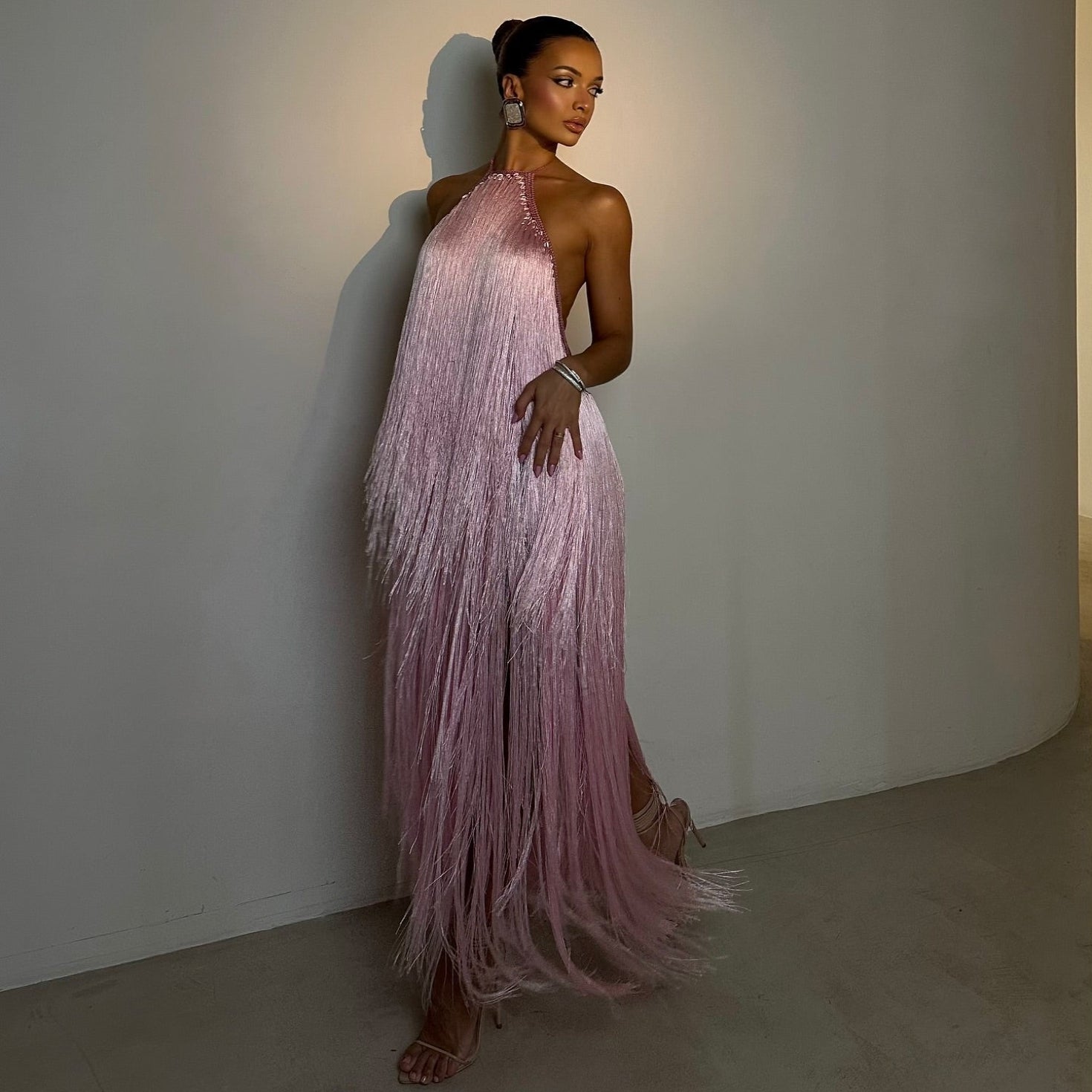 Woman in a pink fringe dress standing against a plain wall.