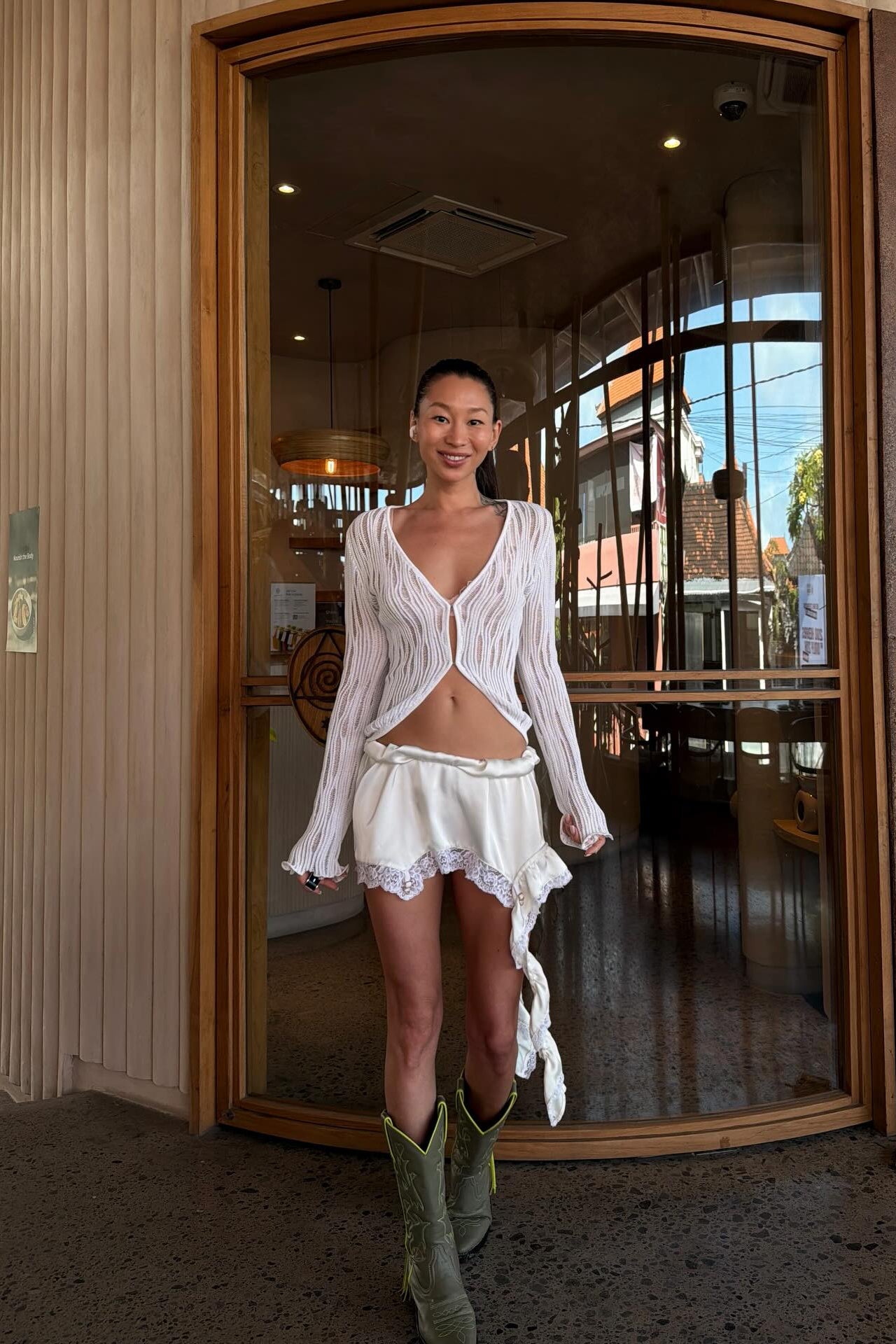 Model wearing white satin mini skirt with ruffle detail, side view