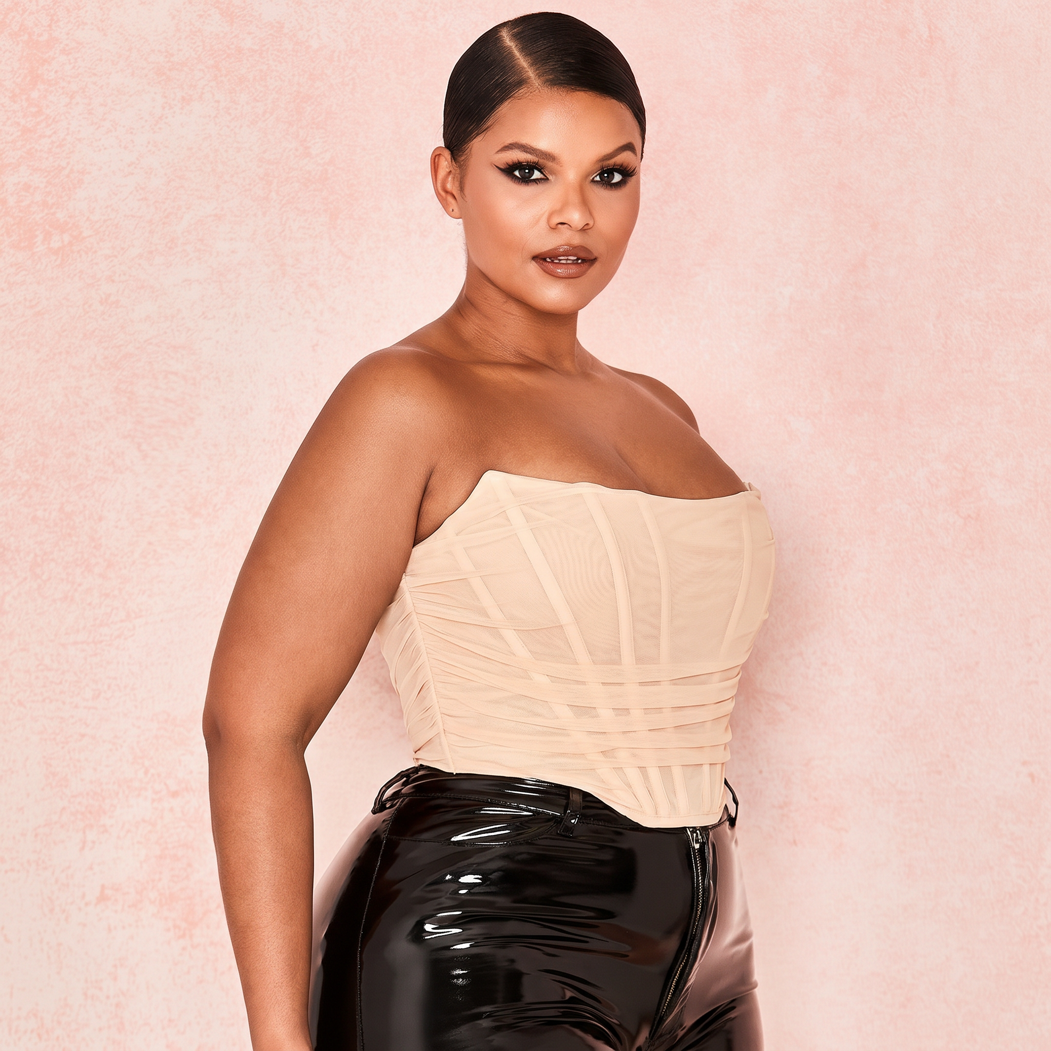 Woman wearing a nude strapless top and black pants against a pink background