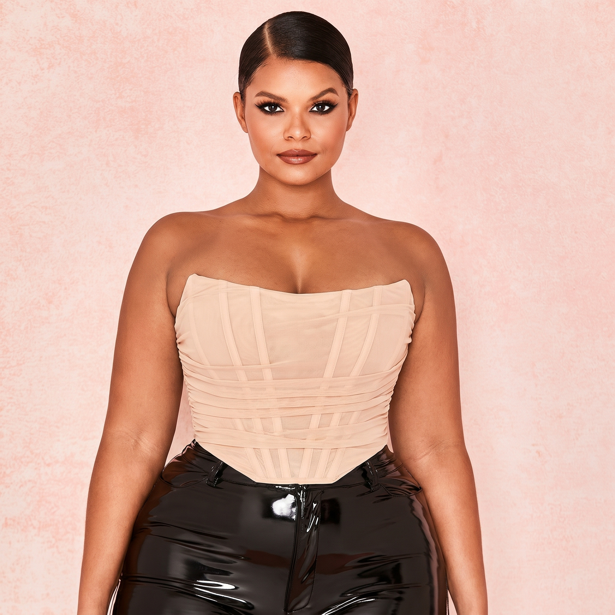 Woman wearing a nude strapless top and black pants against a pink background
