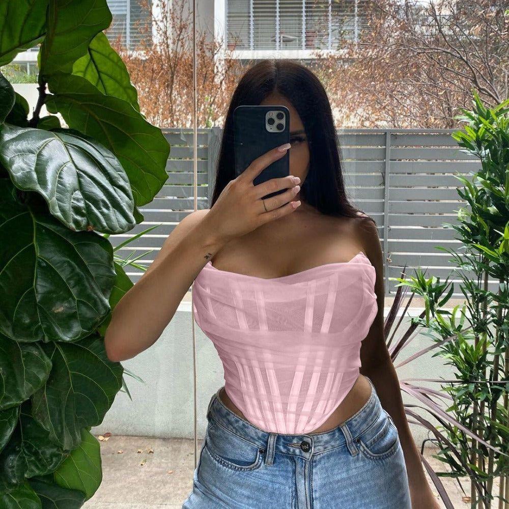 Person wearing a pink top and blue jeans taking a mirror selfie outdoors.