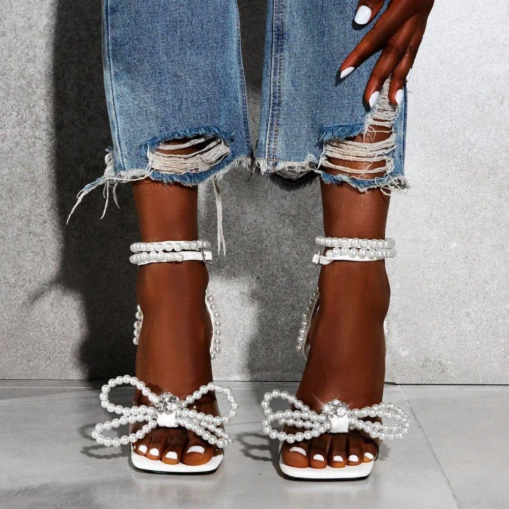 Brown sandals with pearl embellishments worn with ripped jeans on a neutral background