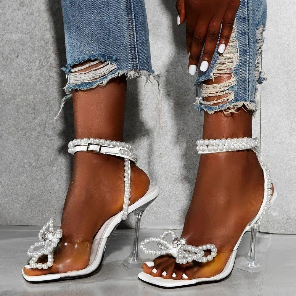 Brown high-heeled sandals with pearl embellishments worn with ripped jeans on a neutral background