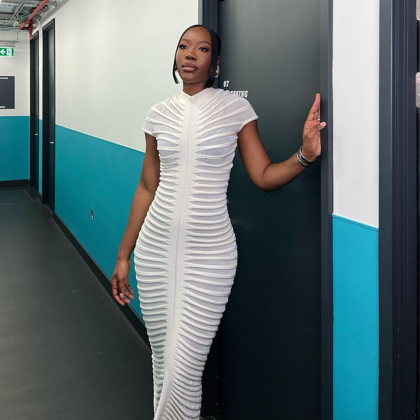 Woman in a white dress standing in a hallway with blue and gray walls.
