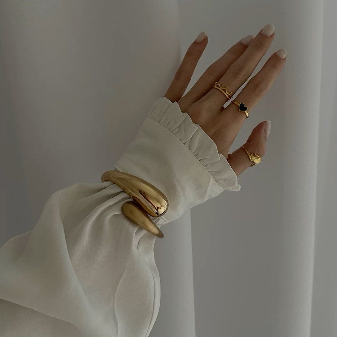 Flared long-sleeve blouse with ruffled cuffs, paired with gold statement rings, elegant styling
