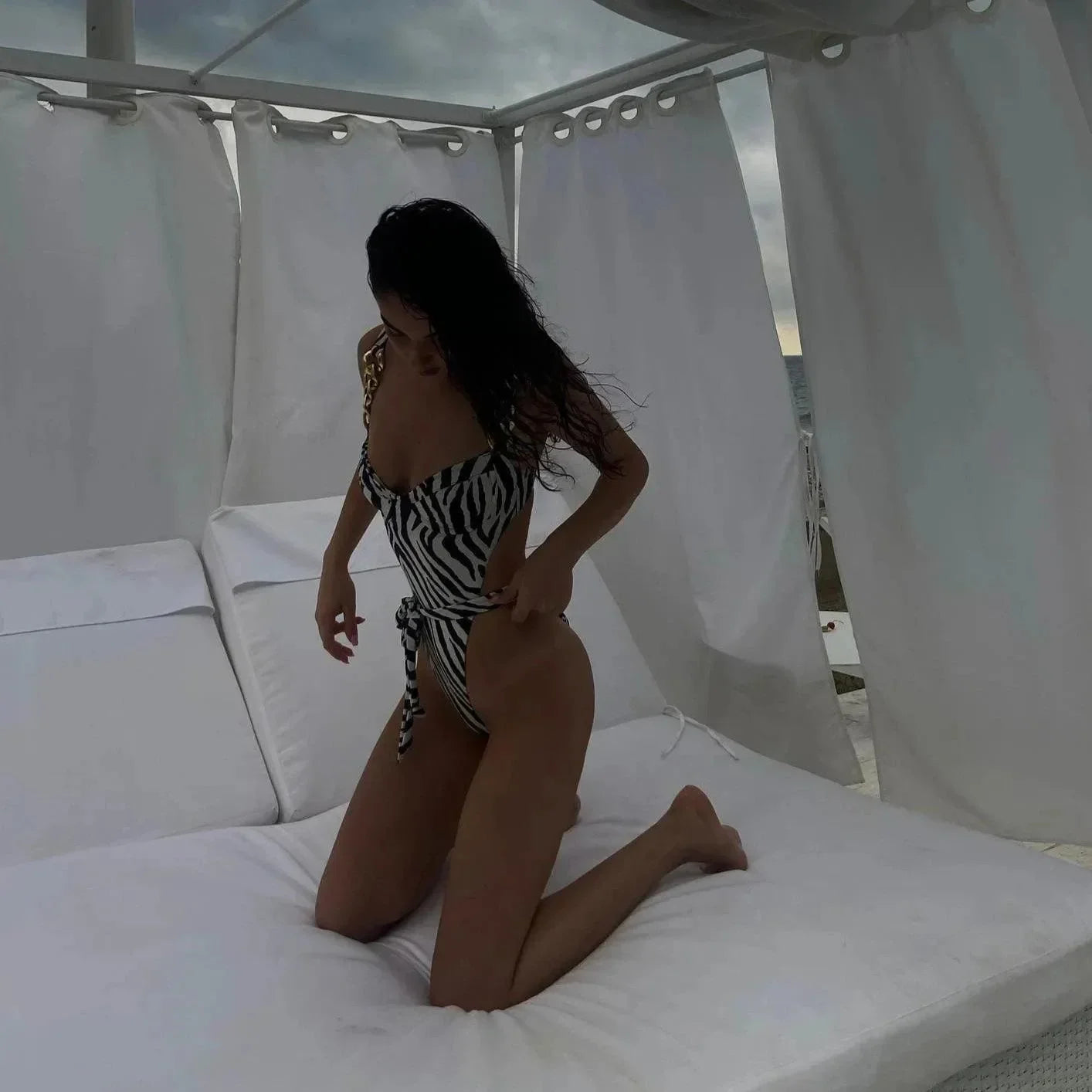 Zebra print one-piece swimsuit with chain details, styled with a cheeky cut, perfect for a beach day or poolside lounging.