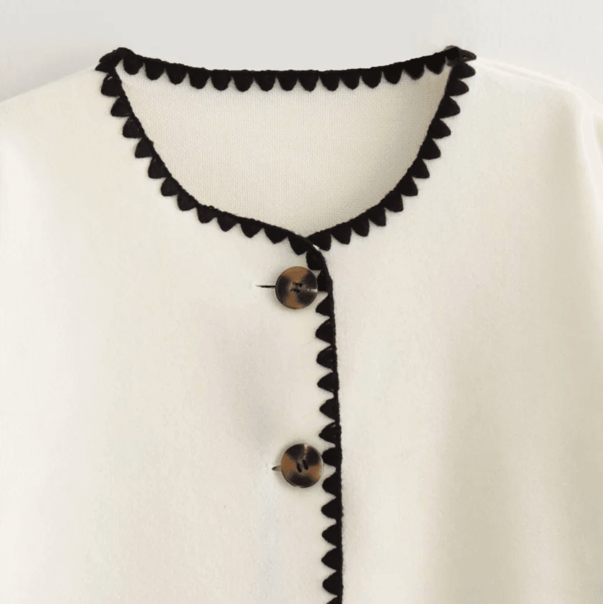Ivory button-up jacket featuring black scalloped trim, styled with a relaxed fit for casual elegance.
