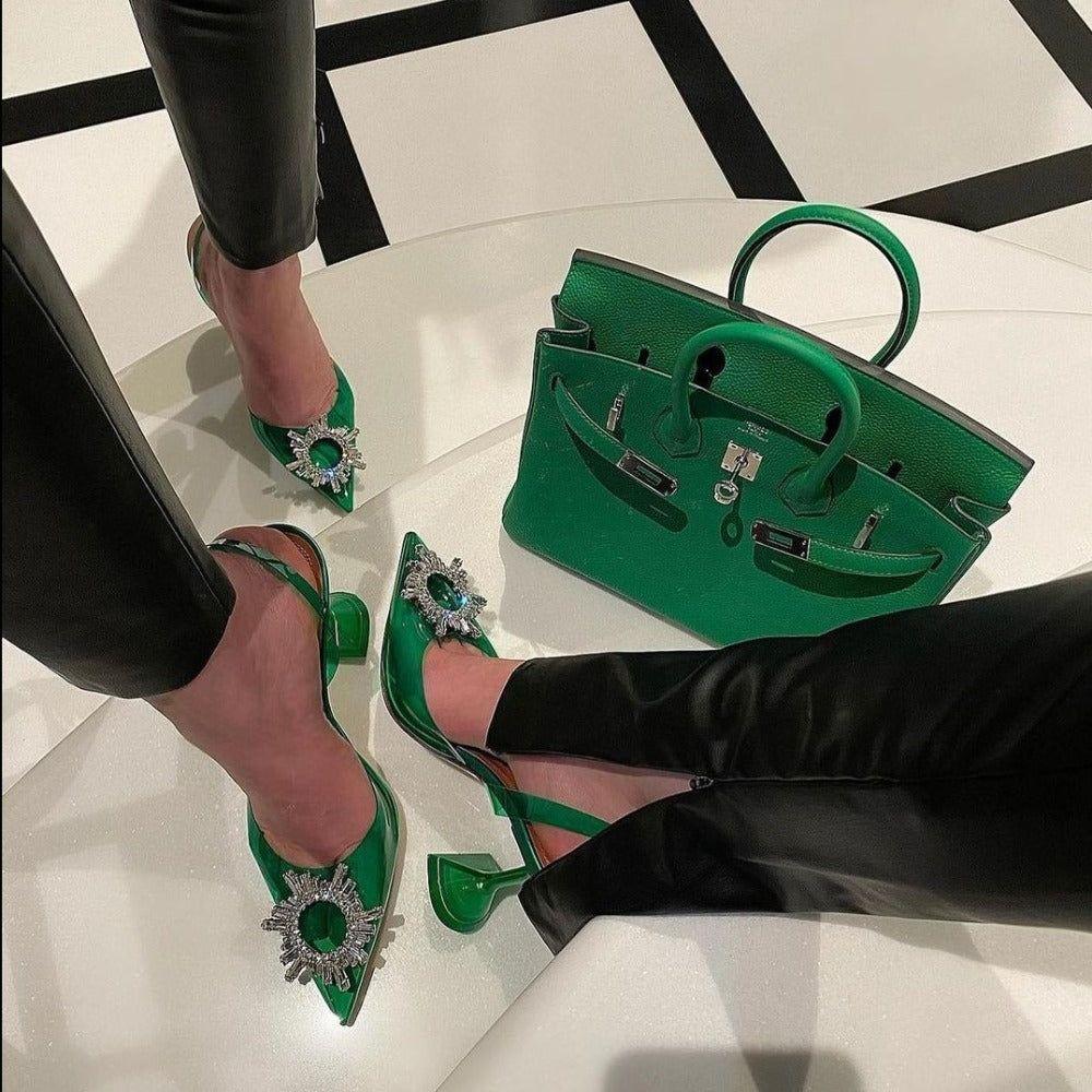 Green high-heeled shoes with embellishments and a matching handbag on a checkered floor.