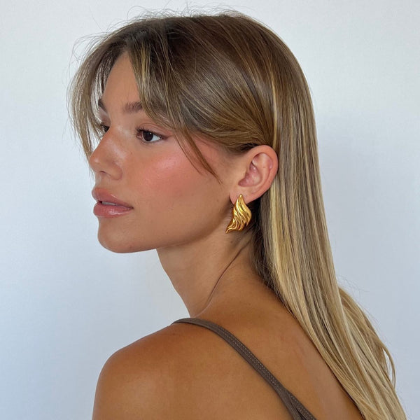 Gold leaf-shaped statement earrings, elegant accessory for evening wear.