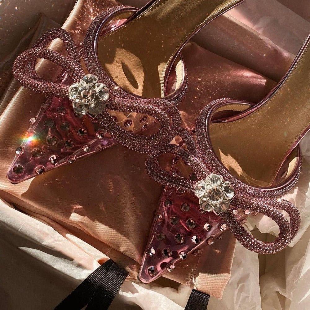 Pink high-heeled shoes with embellishments on a reflective surface