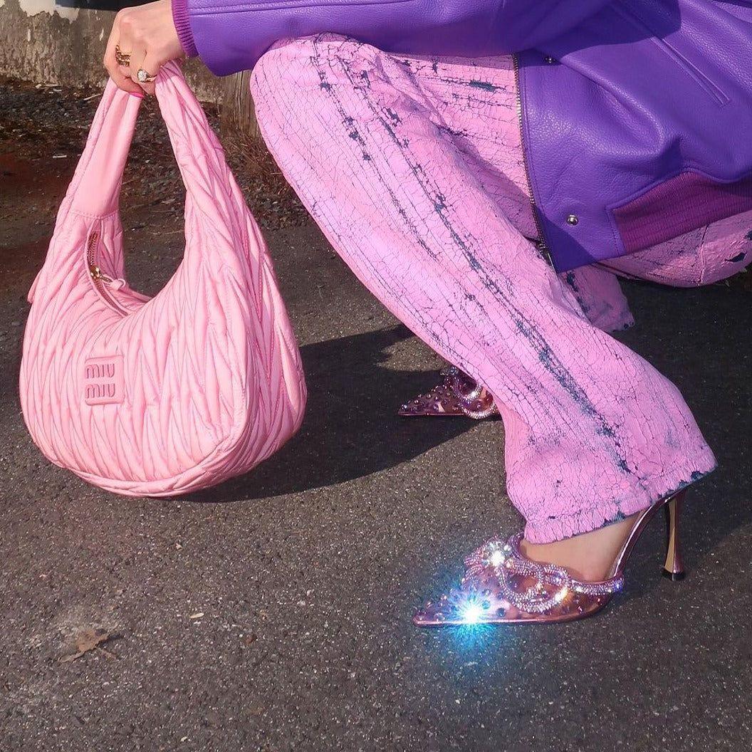 Person wearing a purple jacket and pink pants, holding a pink handbag with glittery shoes.