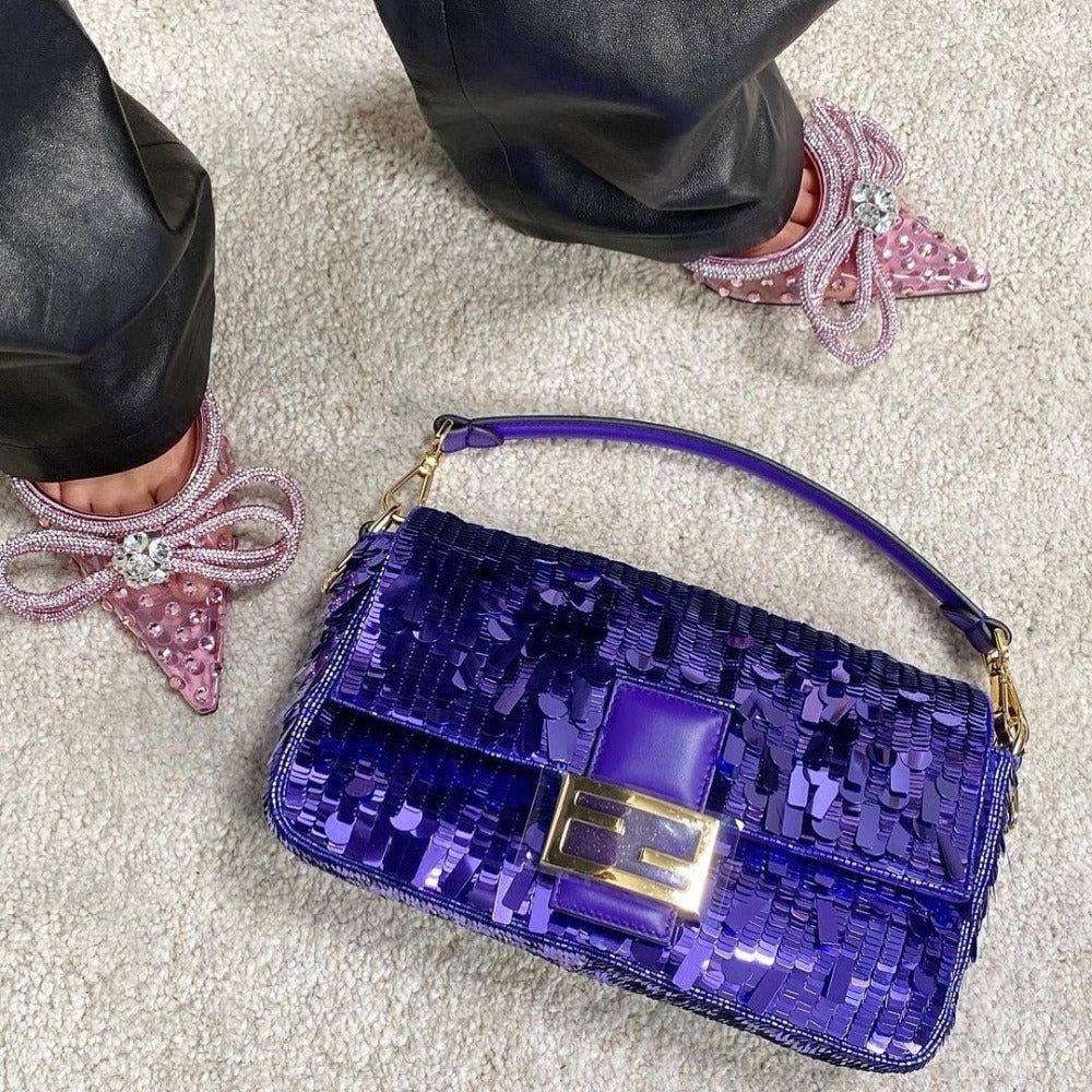 Purple sequin handbag on a light gray carpet with pink shoes featuring bows.