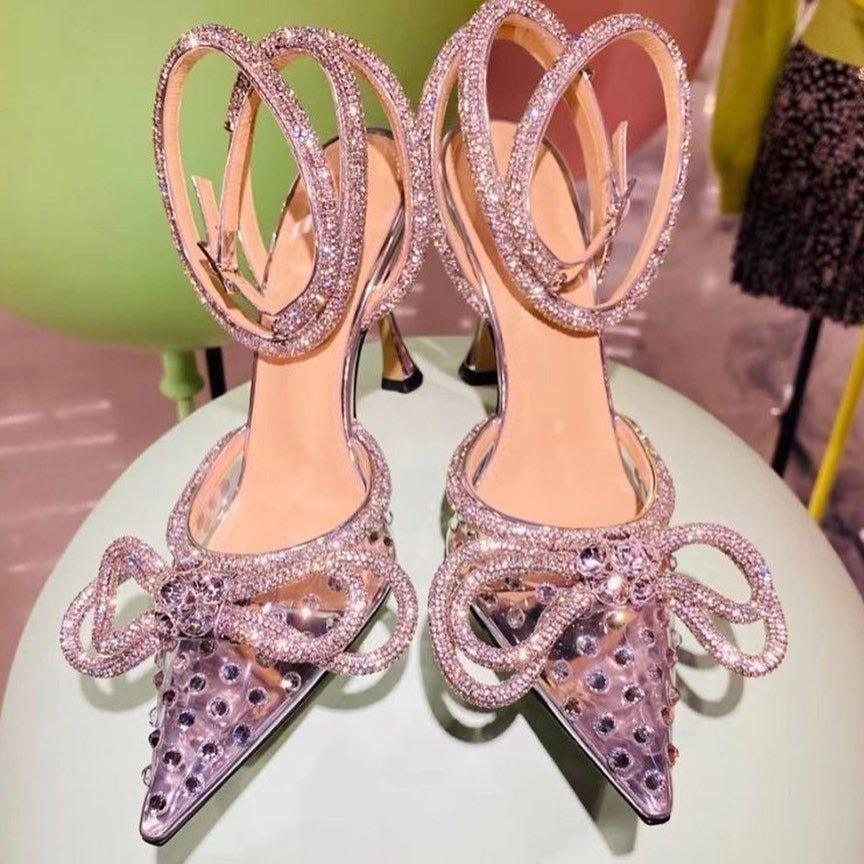 Pair of high-heeled shoes with decorative straps and bows on a light green surface.