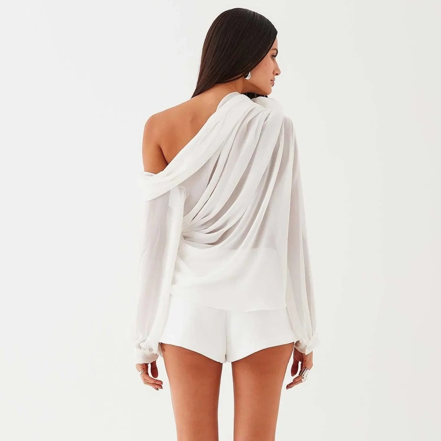 White asymmetrical draped blouse with delicate shoulder detailing, styled off one shoulder for an elegant look.