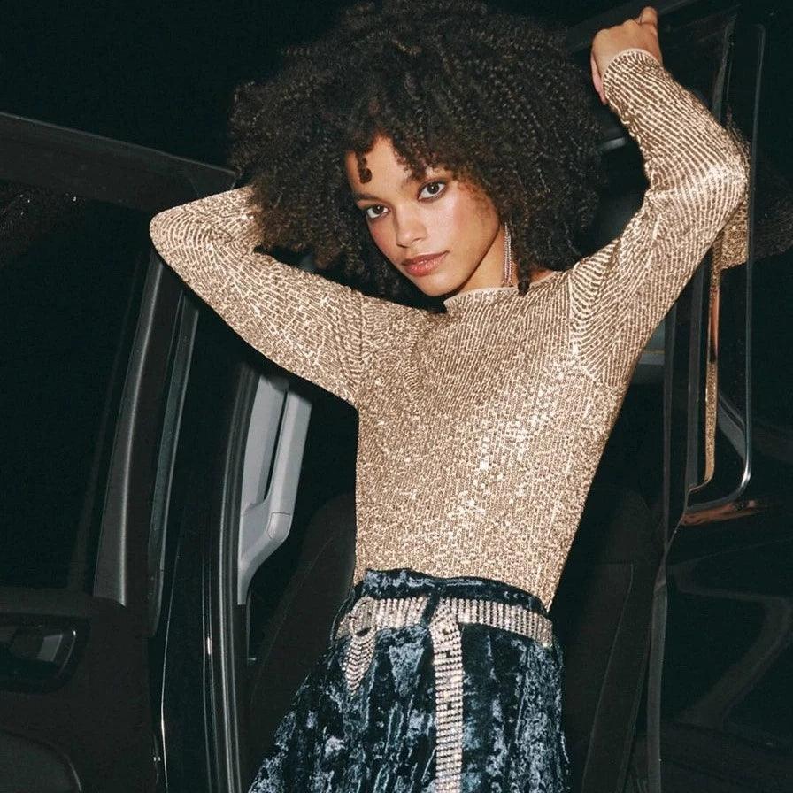 Gold sequined long sleeve top featuring a high neckline, styled with a velvet skirt for a chic, glamorous look.