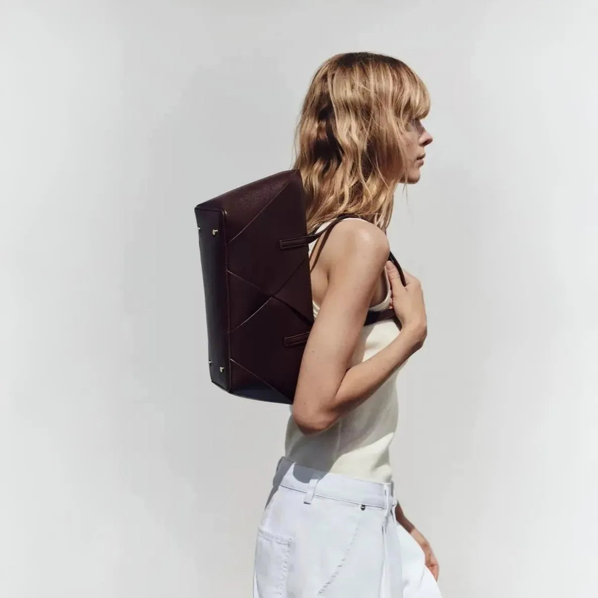 Brown leather tote bag over shoulder, paired with white tank and pants.