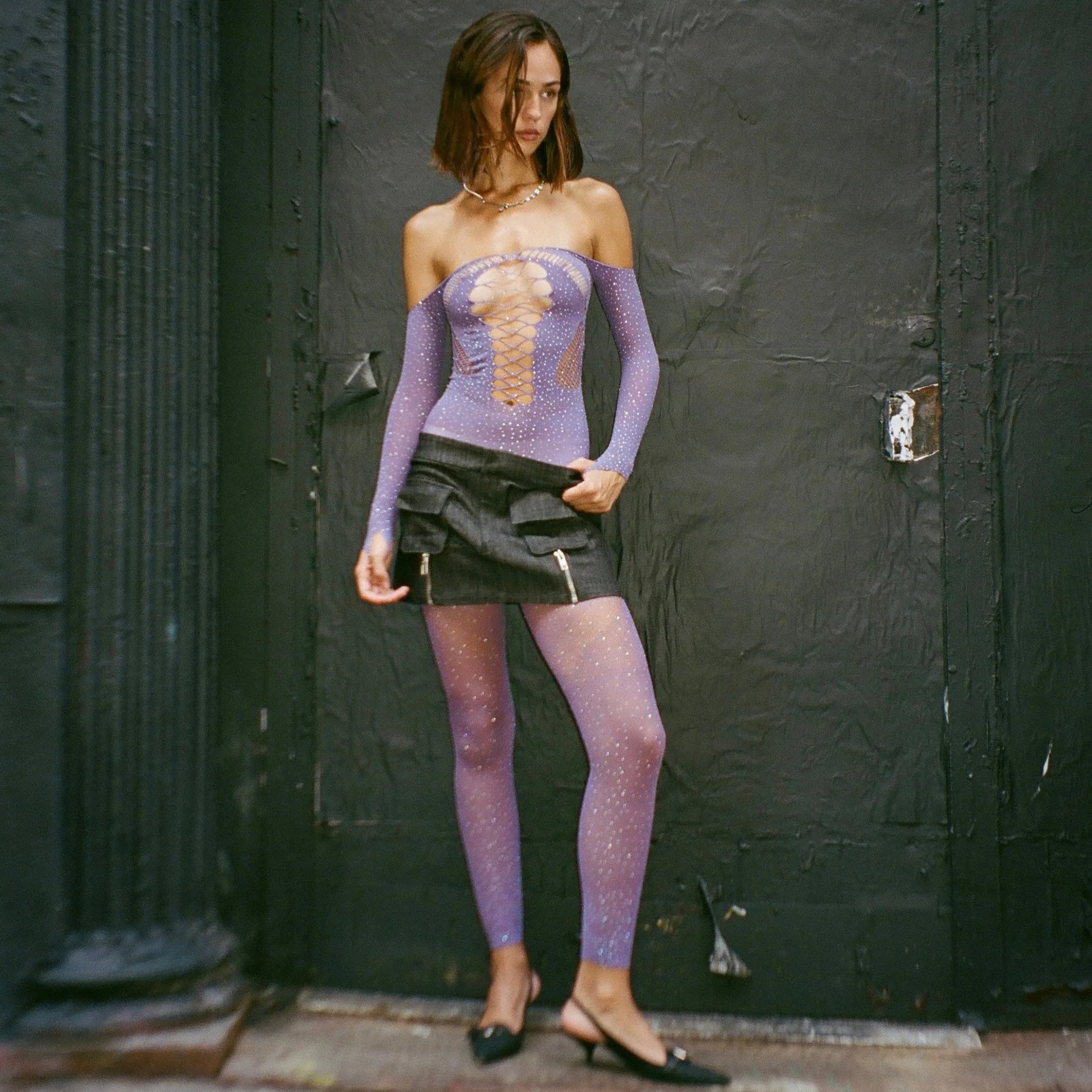 Strappy purple jumpsuit with rhinestone embellishments, off-shoulder design, styled with a chic black mini skirt.