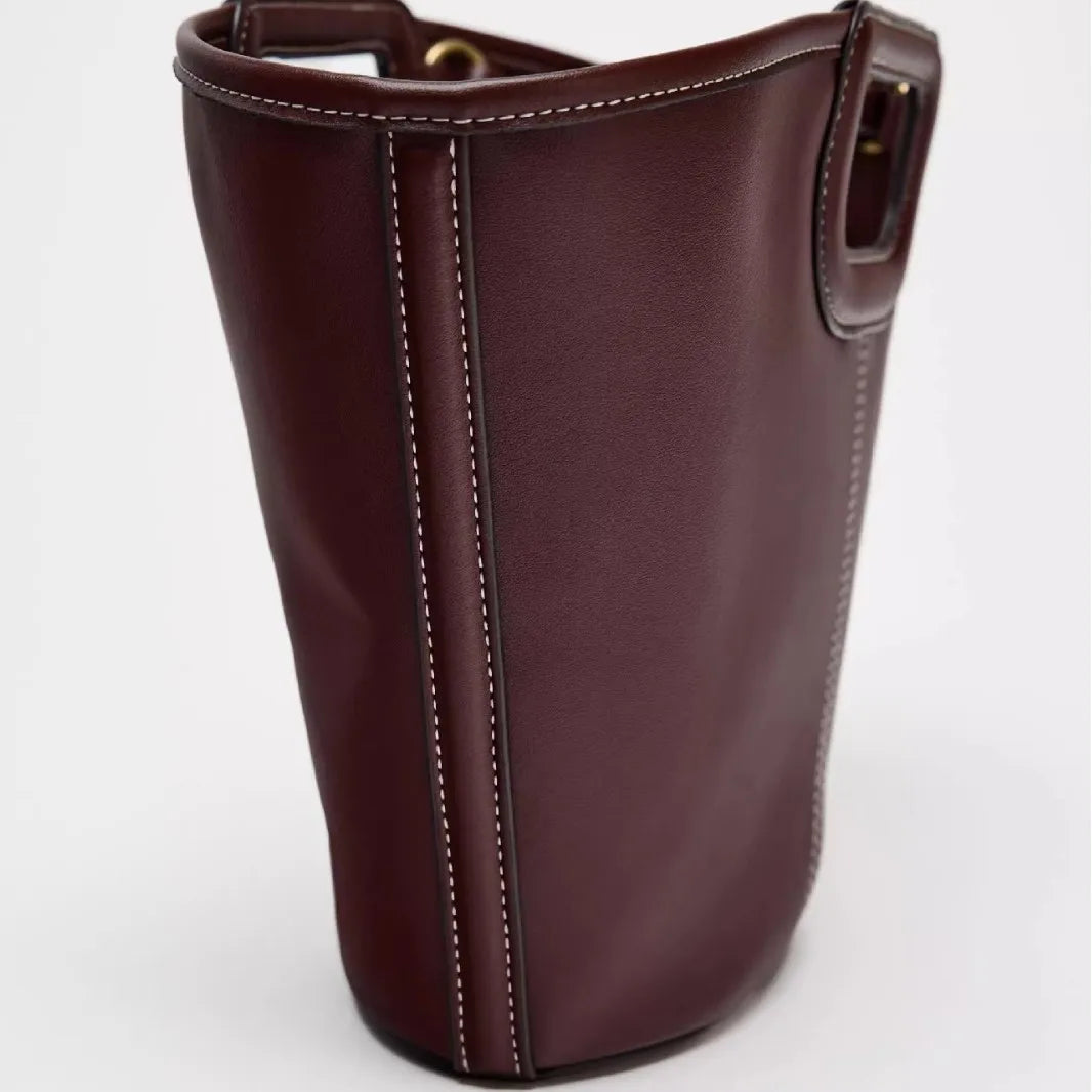 Burgundy leather bucket shoulder bag with contrasting white stitching, styled for a chic, casual look.