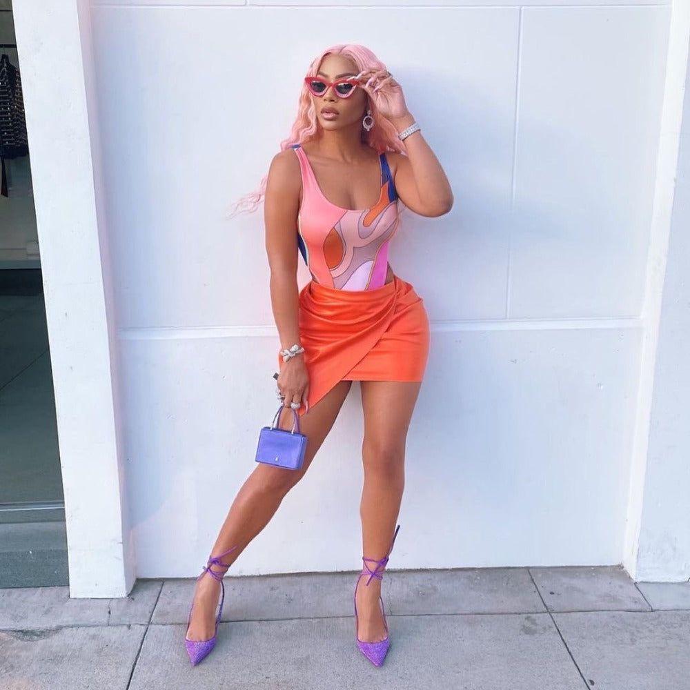 Woman in colorful outfit with pink hair against a white wall