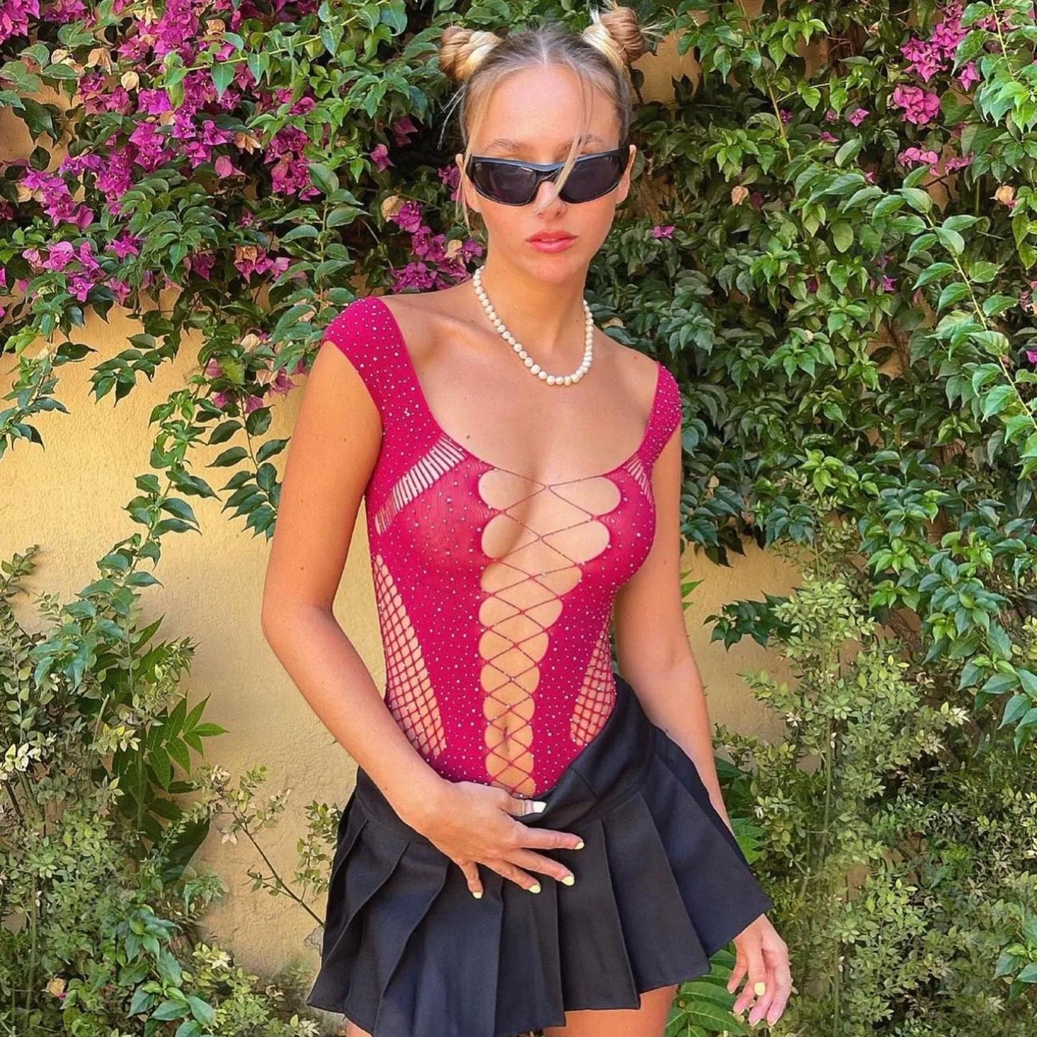 Rhinestone-embellished red bodysuit with crisscross design, styled with a black mini skirt and accessorized with sunglasses.